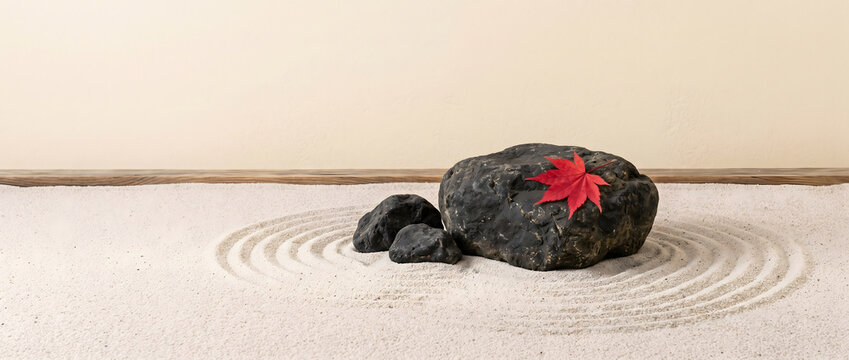 Zen garden with raked sand patterns featuring a red maple leaf resting on dark stones
