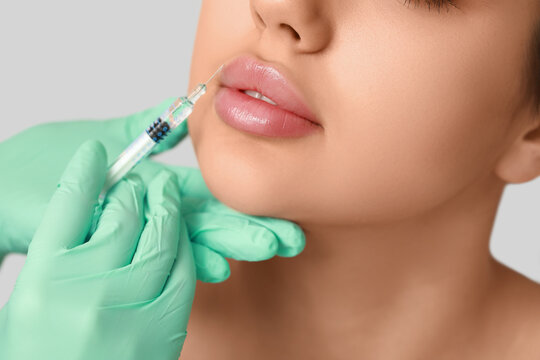 Young woman receiving lip injection on grey background, closeup