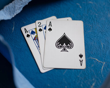 Three playing cards on a blue surface with ace and two of spades