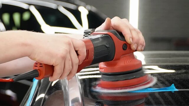 Professional Worker Buffing the Body from Light Scratches, Removing Swirls, Paint Defects from a Body of the Vehicle. A car service worker polishes the black car body with eccentric polishing machine.