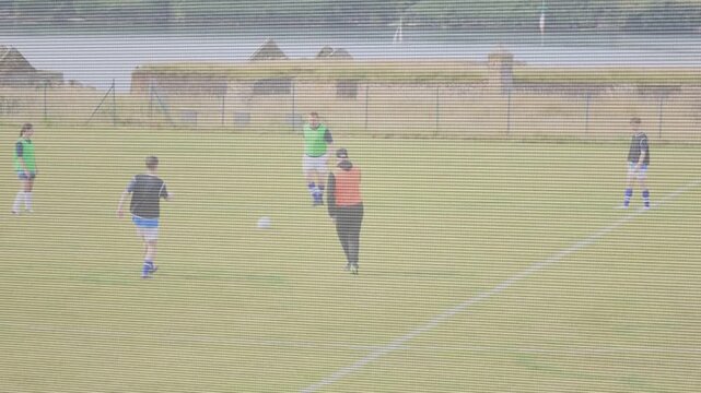 Central coach in orange bib stepping after left player passing ball, guiding football training