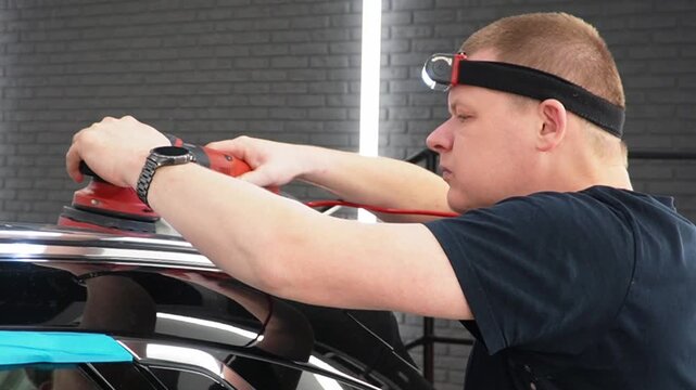 Professional Worker Buffing the Body from Light Scratches, Removing Swirls, Paint Defects from a Body of the Vehicle. A car service worker polishes the black car body with eccentric polishing machine.