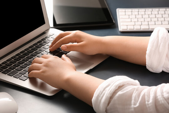 Female programmer typing on laptop keyboard at her workplace in office, closeup