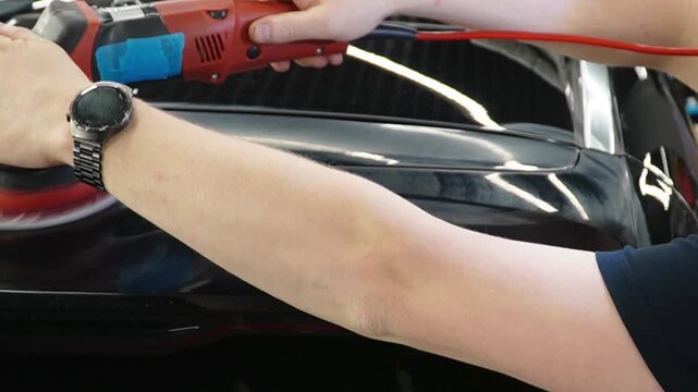 Professional Worker Buffing the Body from Light Scratches, Removing Swirls, Paint Defects from a Body of the Vehicle. A car service worker polishes the black car body with eccentric polishing machine.