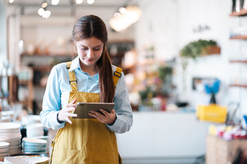 Woman using tablet in small shop interior, retail worker in apron with focused expression © chokniti