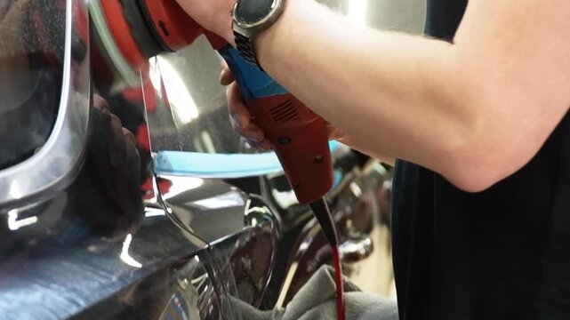 Professional Worker Buffing the Body from Light Scratches, Removing Swirls, Paint Defects from a Body of the Vehicle. A car service worker polishes the black car body with eccentric polishing machine.