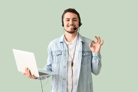 Male technical support agent with laptop showing OK on mint background