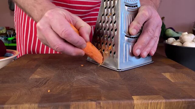 Chef grating carrot on a metal shredder preparing fresh ingredients for healthy cooking and culinary dish.