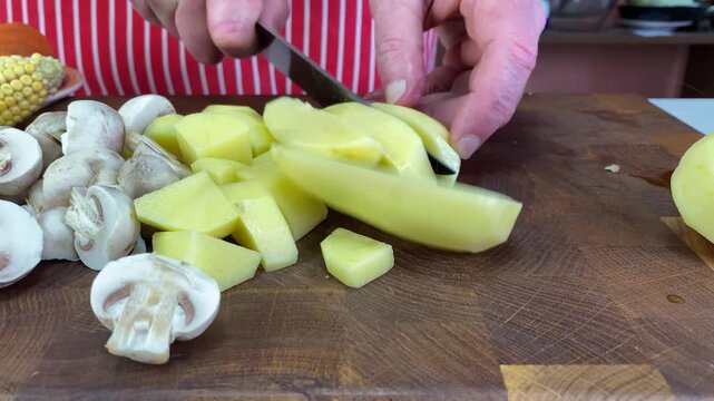 Chefs hands slicing potatoes and whole mushrooms on a cutting surface, preparing wholesome food for a meal.