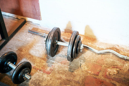 Weightlifting equipment including dumbbells and a barbell with weight plates on a concrete floor