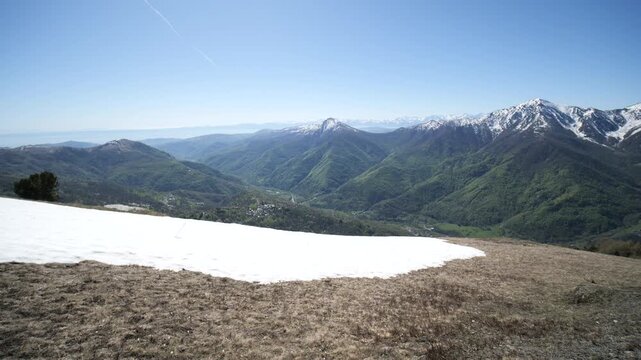 Panorama: wide landscape of Valle Varaita with Monviso massif in Italian Alps, green meadow and snow-capped peaks under clear blue sky in springtime mountain scenery