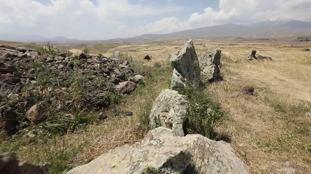 Camera pans across ancient standing stones in a mountainous landscape, revealing a close-up of a distinctive circular hole bored through a rough megalith at Zorats Karer, Armenia.