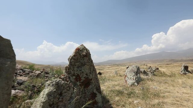 Camera pans across ancient standing stones in a mountainous landscape, revealing a close-up of a distinctive circular hole bored through a rough megalith at Zorats Karer, Armenia.