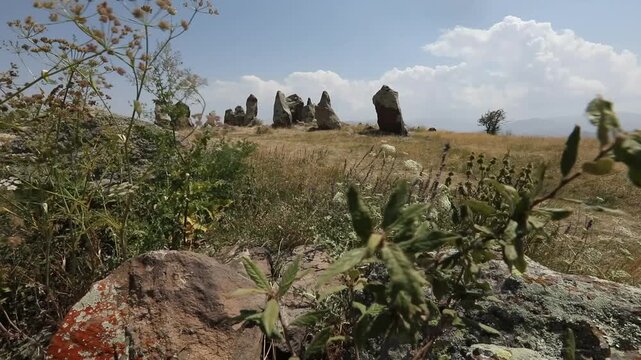 Camera pans across ancient standing stones in a mountainous landscape, revealing a close-up of a distinctive circular hole bored through a rough megalith at Zorats Karer, Armenia.