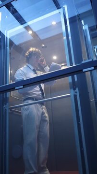 Vertical screen businessman talks with client in elevator using headset and reviewing document showing focused communication business negotiation and professional workflow
