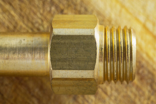 Close-up macro shot of a brass threaded pipe fitting on a wooden background