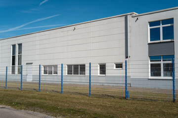 Naklejka premium White industrial building with security fence under blue sky
