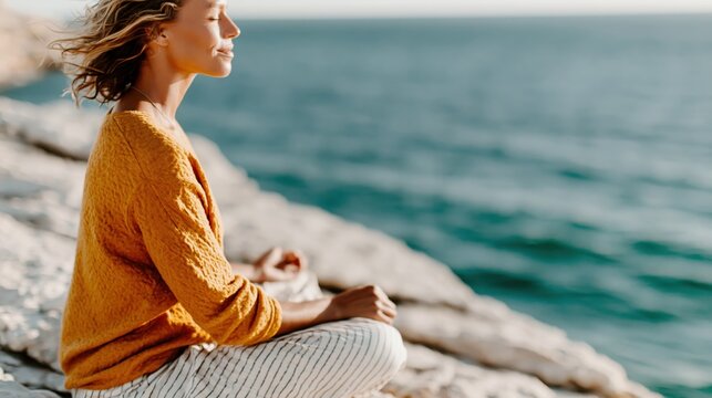 A serene woman meditating by the seaside, harmonizing with nature and reflecting inner peace as the waves gently lap against the rocks in the background.