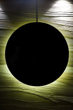 Modern minimalist wall art with black circular object and backlight, abstract rough texture background for contemporary interior design.