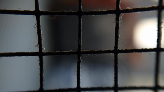 Metal wire fence with grid pattern, rusty frame and blurred window light, security barrier, industrial building exterior
