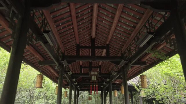 Traditional Chinese pavilion corridor with red lanterns, wooden beams, and cultural architectural details in a peaceful garden.