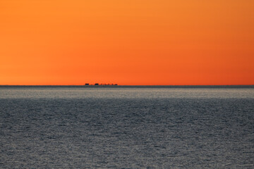 Fototapeta premium Distant cargo ship silhouette appearing on the horizon of the Baltic Sea during a vibrant orange sunset, mirage effect