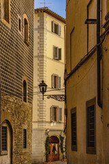 Fototapeta premium Historic Narrow Florentine Street Alley In Italy With Ancient Stone And Sgraffito Building Facades A Lamp Post And Traditional Wooden Shutters Under A Warm Evening Sky