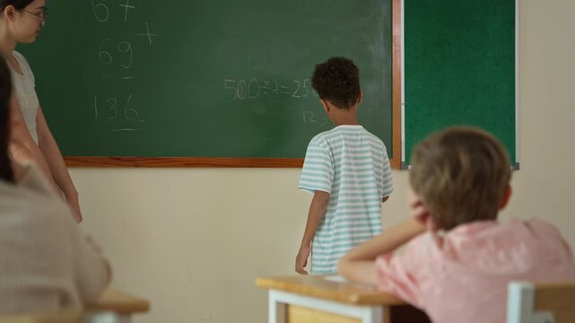 Schoolgirl solving math problem on chalkboard with teacher guidance in classroom, representing education and problem solving