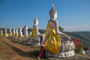 Obraz premium Woman In Traditional Attire Placing A Golden Robe On A Buddha Statue At A Peaceful Mountain Temple
