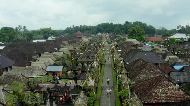 Galungan, Indonesia - 15 April 2026: Aerial view of a traditional Balinese village with thatched roofs and bamboo decorations along a central path in Bali.