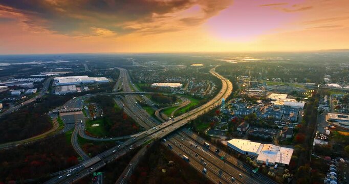 Hectic traffic on the highways and multi-lane motorways crossing the vast cityscape. Setting sun colors the scenery and cloudy sky.