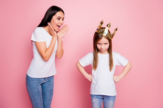 Mother cheering as daughter wears a gold crown and strikes a proud, playful pose on pink background &mdash; family moment of confidence, pretend play and young princess fun