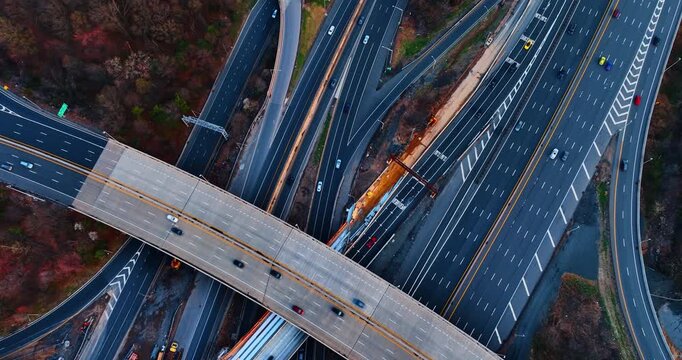 Descend over the bridge across the multi-lane parallel highways. Lots of cars go by the roads surrounded by the woods.