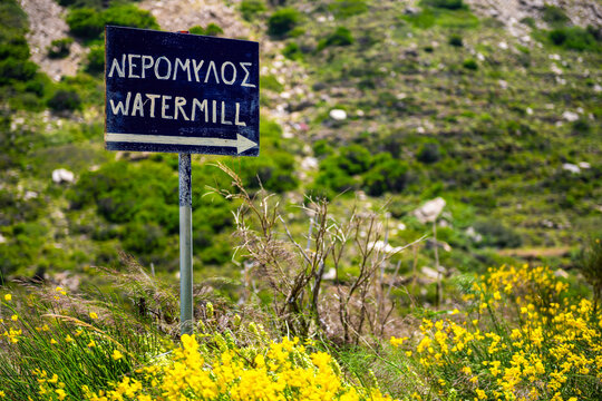 Sign for Aris river old watermill at fishing coastal village of Karavostamo on Ikaria island, Greece with stone fence