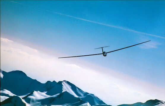 White Glider Sailplane Soaring Over Snow Capped Mountain Peaks Against a Clear Blue Sky with Vapor Trail