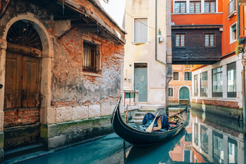 Narrow Venice canal with gondola and aged buildings. Intimate historic alley with calm water reflections in Italy © Viktoriya