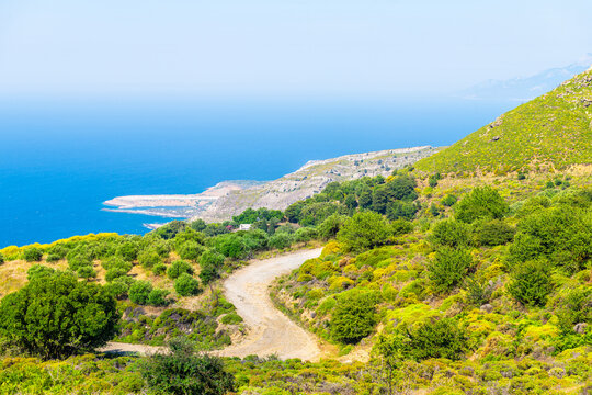 Perdiki village at Ikaria island northern shore coast, Greece with Faros airport runway, farm garden building by street road