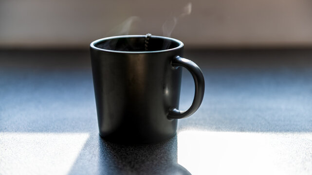 One tea or coffee cups with hot drink, steam rising at morning breakfast by window at home house kitchen macro closeup