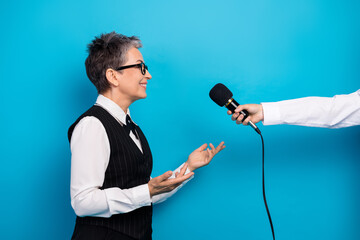 Naklejka premium Mature businesswoman being interviewed on a blue studio backdrop with microphone in a professional setting