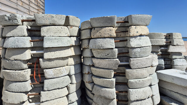 Tall stacks of curved concrete blocks reinforced with rusted metal bars sitting outdoors under a clear blue sky.