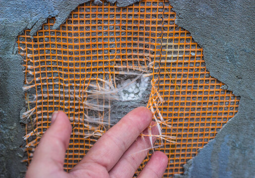 Hand testing orange fiberglass reinforcing mesh on a damaged concrete wall.