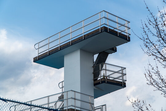 Modern multi-level high diving board structure at an outdoor swimming pool against a bright blue sky with wispy clouds, ready for summer aquatic sports and recreational fun.