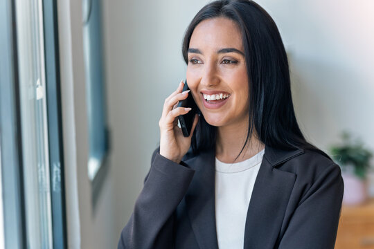 Smiling businesswoman talking with smartphone while standing in the office