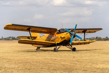 A parked yellow biplane old Soviet-made transport plane on a grassy airfield © ZenitX