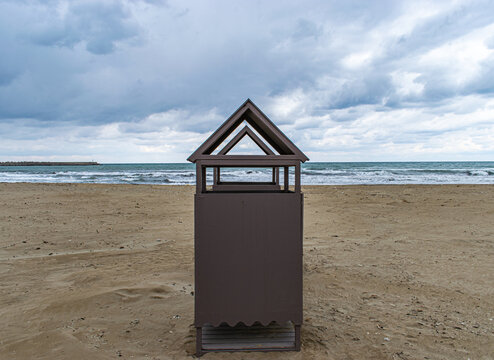 Symmetrical wooden beach hut or changing room on a sandy beach under a cloudy dramatic sky.