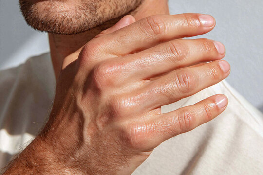 Close up of male fingers catching warm sunlight on textured skin with subtle beard stubble and natural lighting creating luminous highlights and shadow, evoking calm and tactile warmth