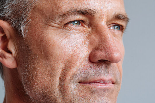 Mature man close up portrait with detailed skin texture and contemplative expression, natural light highlighting wrinkles and blue eye