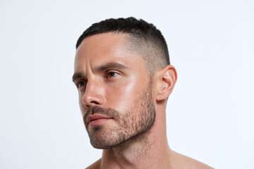 Obraz premium Close up portrait of man with hydrated skin and soft light, showing short haircut, trimmed beard and contemplative expression on neutral background