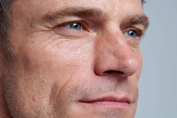 Fototapeta premium Close up male face with detailed pores, skin grain, blue eye and subtle stubble conveying contemplative emotion