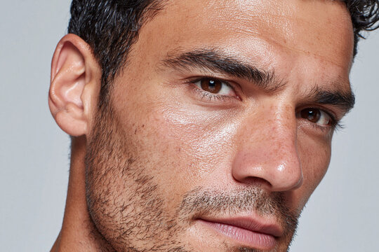 Close up male face hydrated cheek area reflecting skin texture brown eye stubble intense gaze natural light smooth complexion warm tone